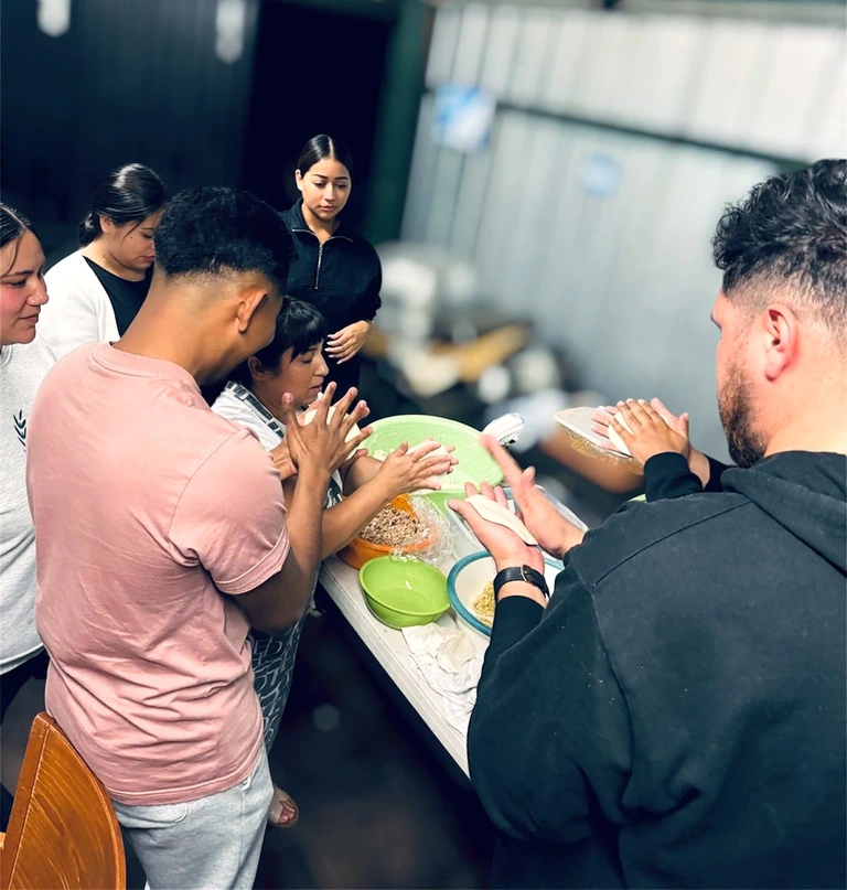 Miembros de la iglesia reunidos alrededor de una mesa preparando alimentos juntos.